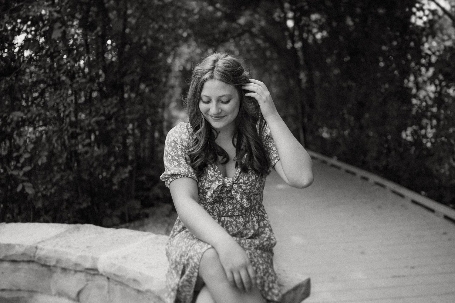 A person in a floral dress sits on a stone wall along a path in a black and white photograph.