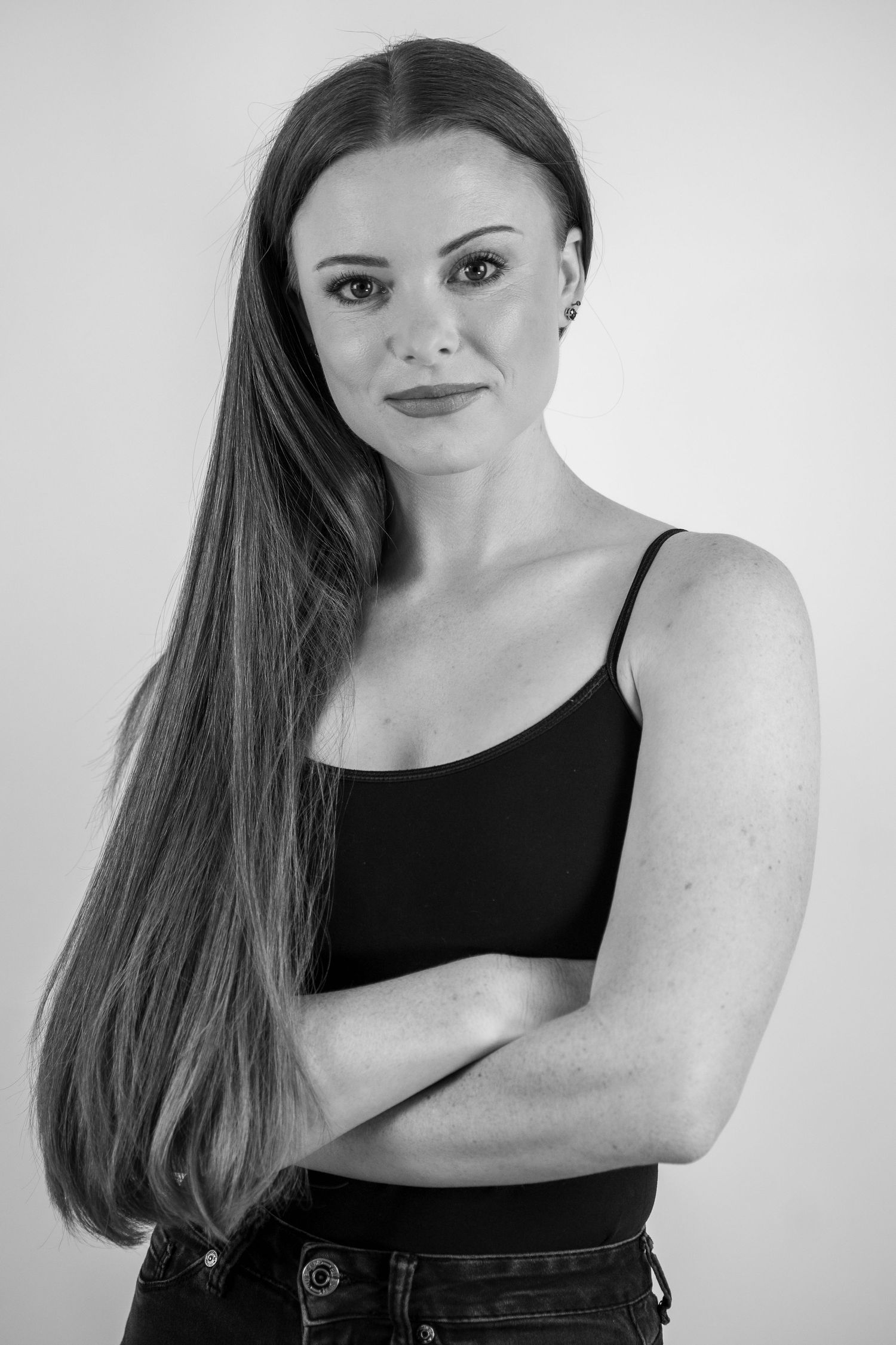 Black and white portrait of person in black tank top with arms crossed against neutral backdrop.