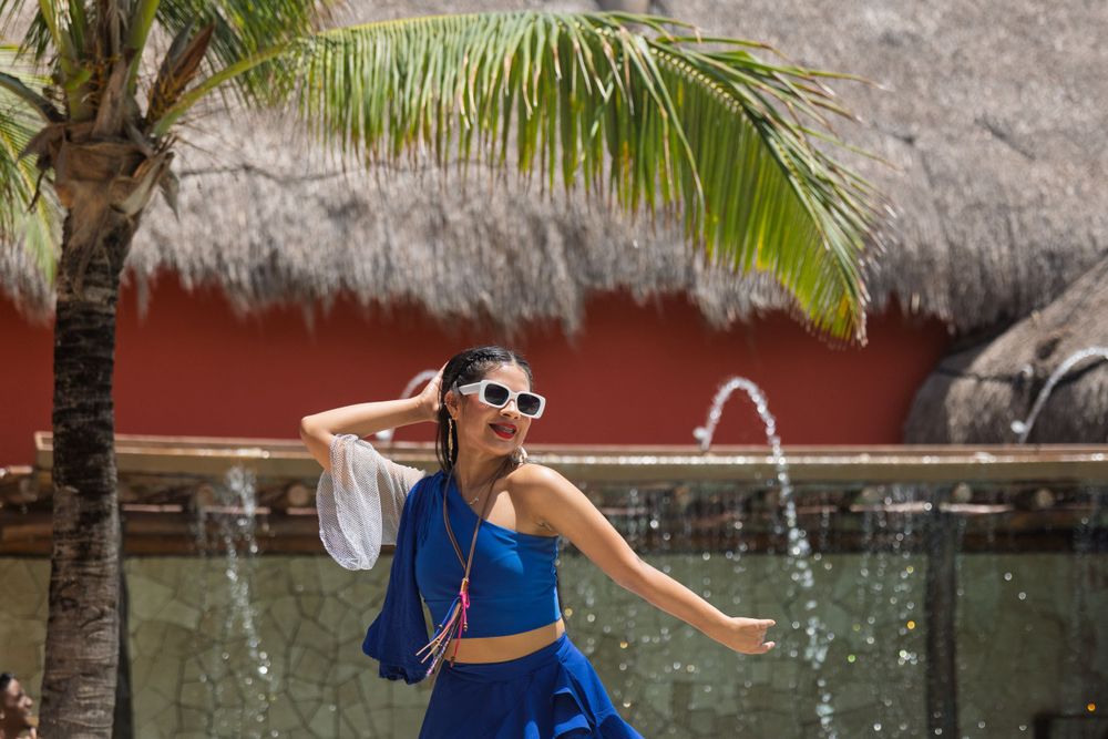 Sunny tropical resort area with palm trees and thatched roof structures.