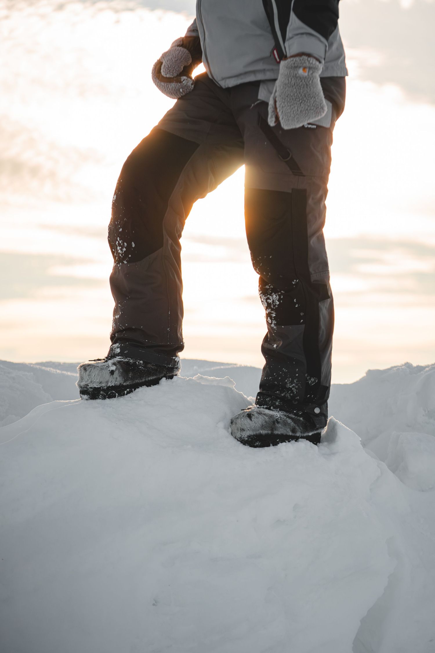 Snow-covered boots standing on white winter peak at sunset.