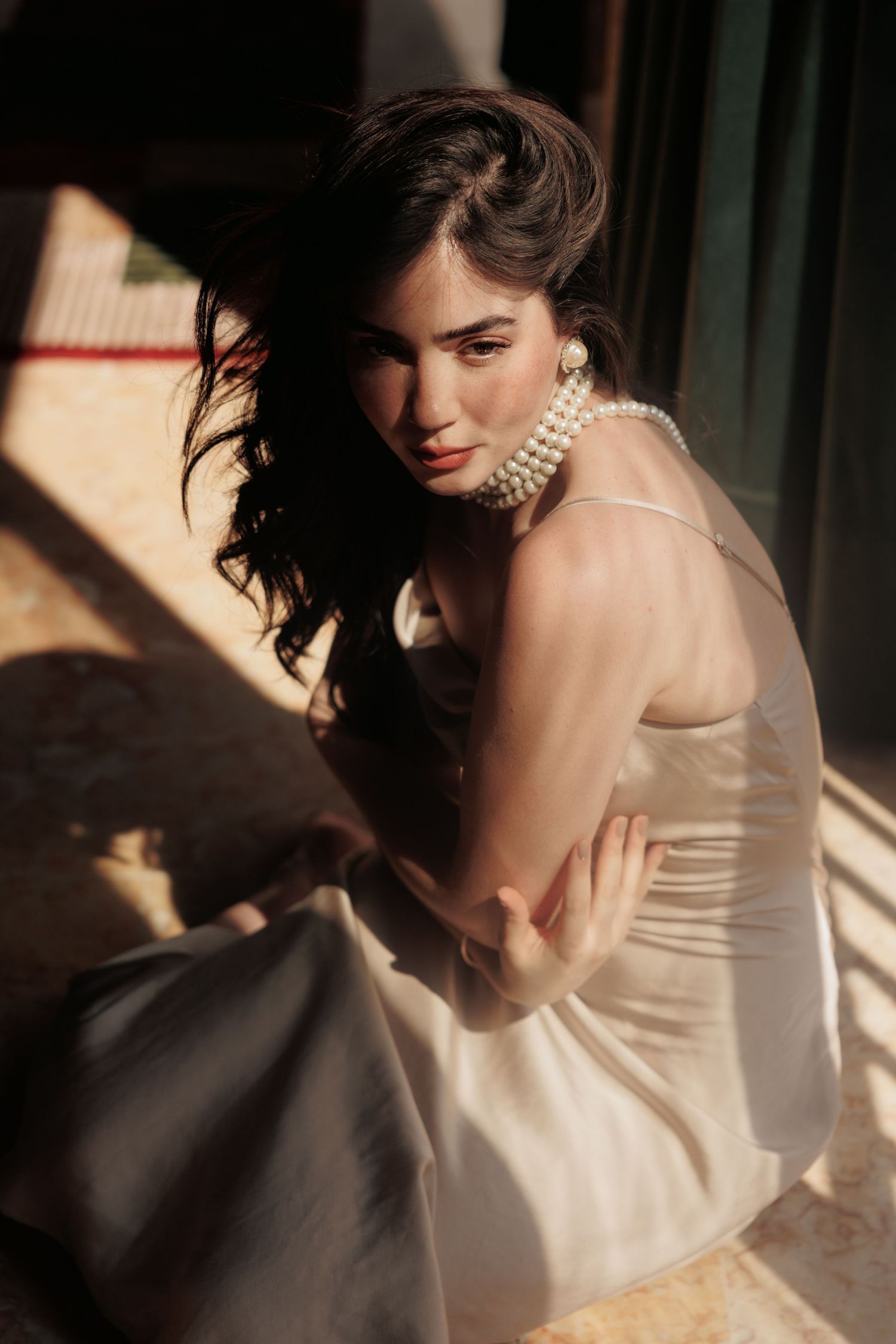 Bridal portrait with pearl necklace and strapless dress in dramatic window light.