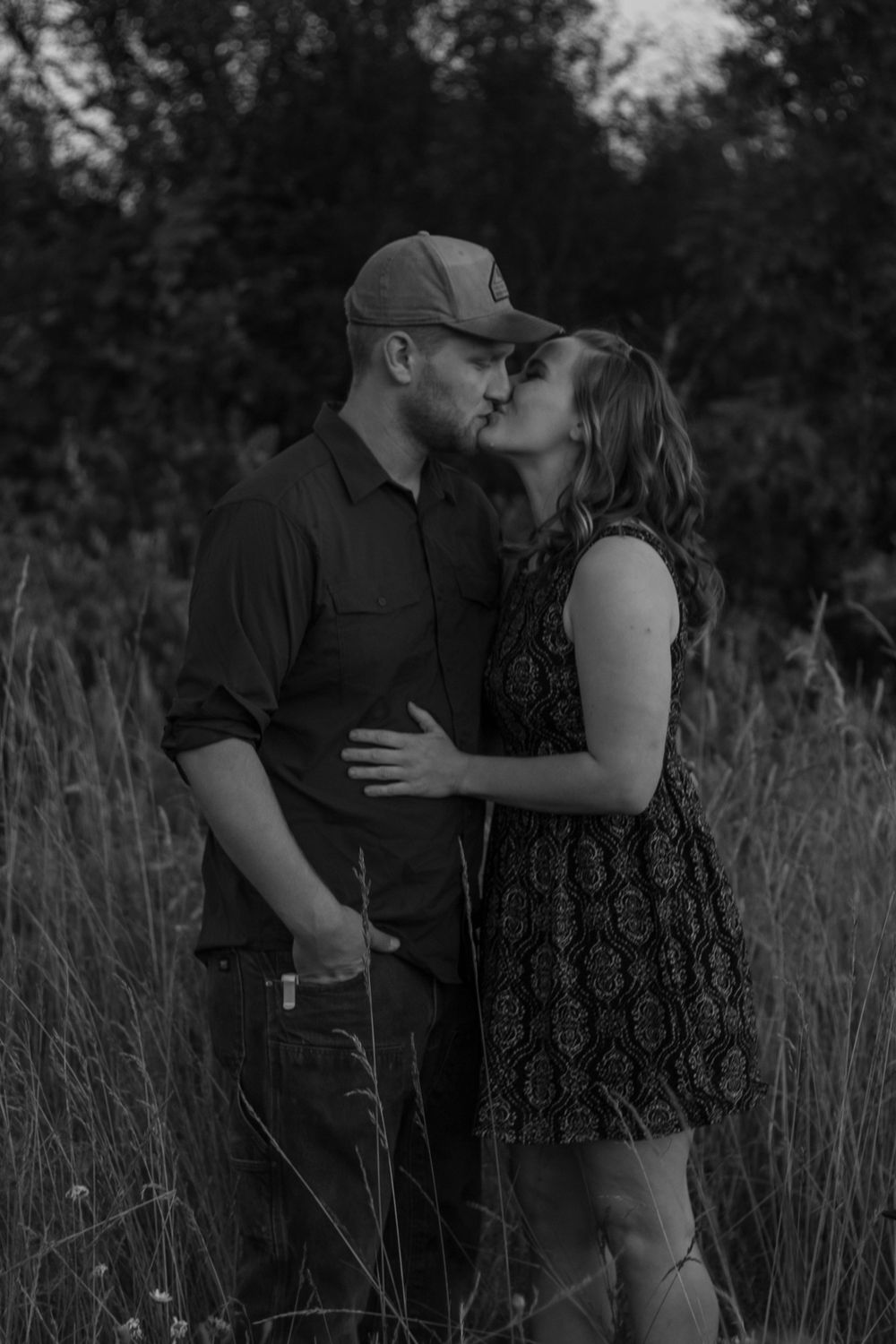 Black and white photo of a couple sharing a kiss in a tall grass field.
