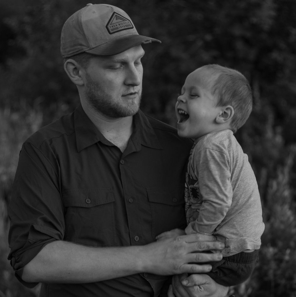 Black and white photo of a father holding his laughing baby outdoors in nature.