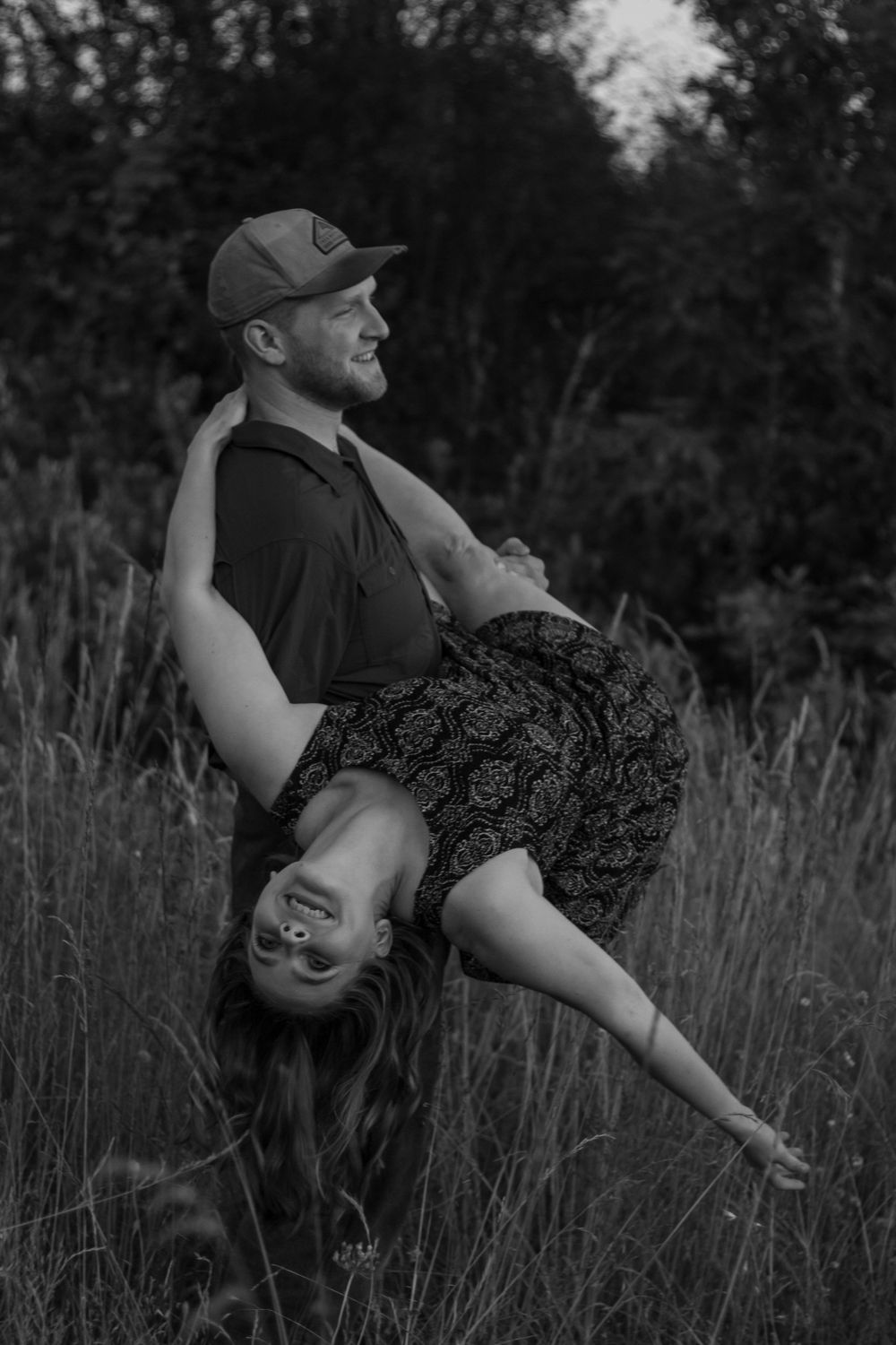 Black and white photo of a man playfully holding a woman upside down in a field.