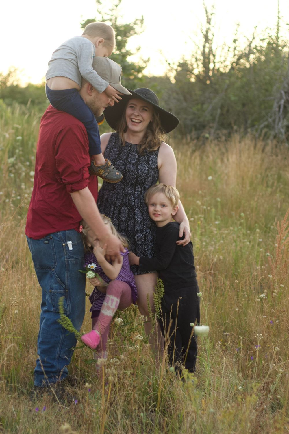 Happy family of four playing together in a sunlit meadow with wildflowers at golden hour.