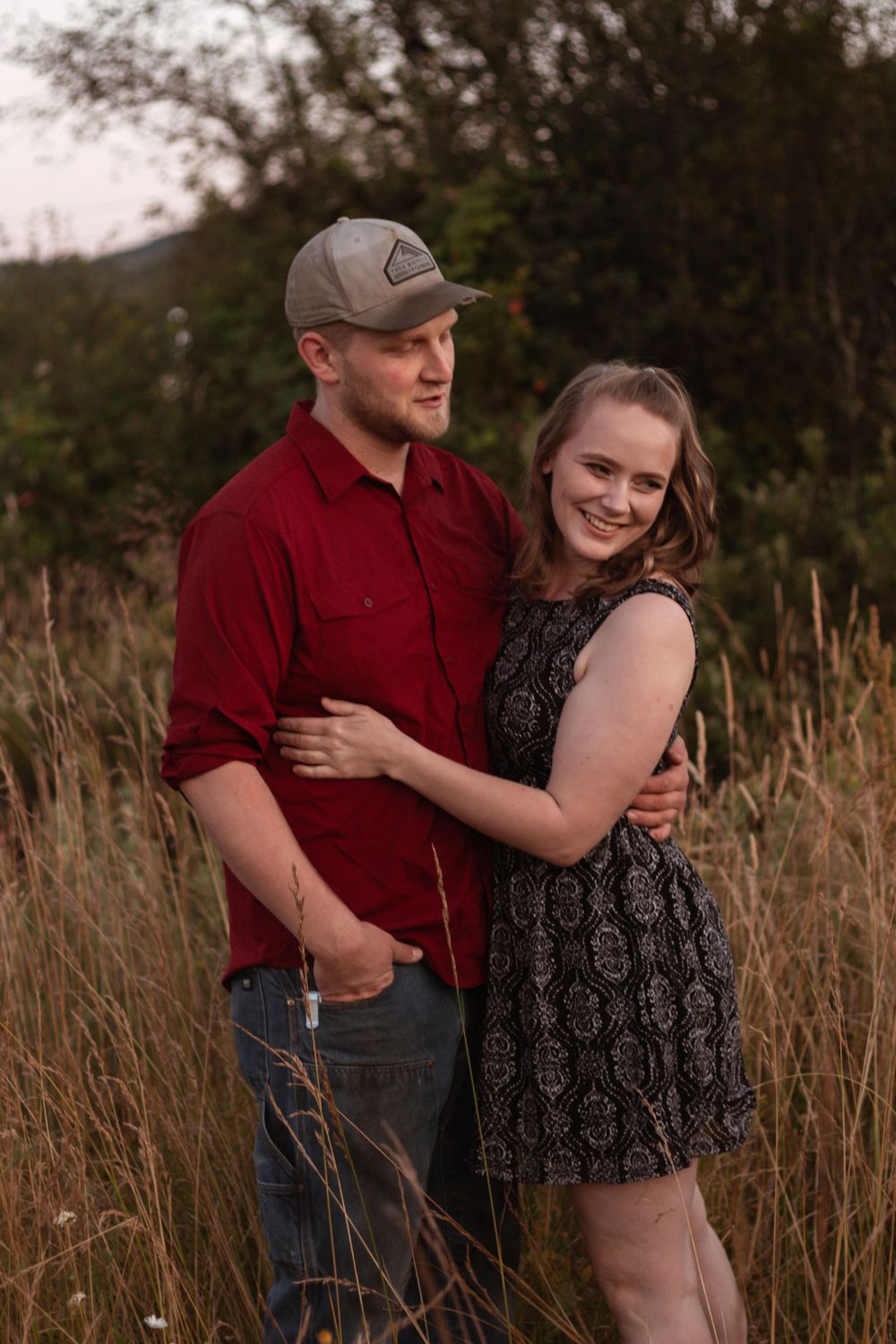 Young couple embraces warmly in a tall grass field during golden hour photography session.
