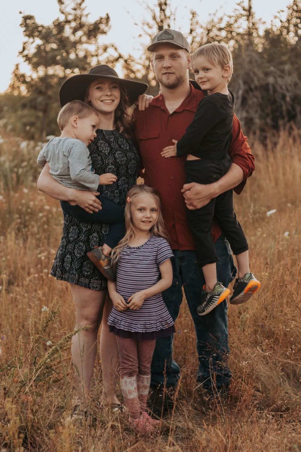 Happy family of five poses together in a golden autumn field at sunset.