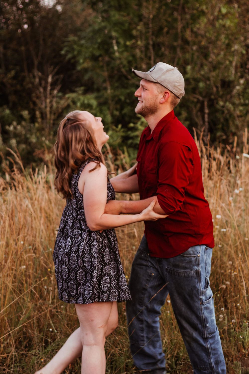Couple dances and laughs together in a sunlit field surrounded by tall golden grass.