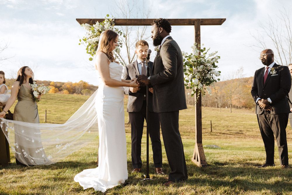 A wedding couple exchanges vows beneath a rustic wooden arch during a fall countryside ceremony near vernon nj.