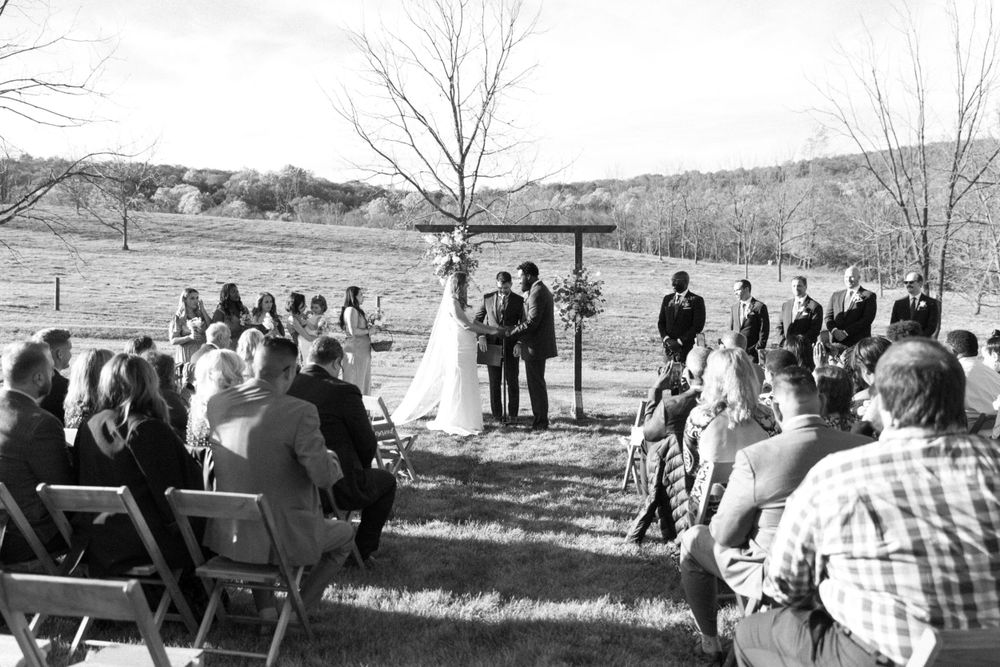 A black and white outdoor wedding ceremony taking place at a rustic venue with guests seated in folding chairs near vernon nj.
