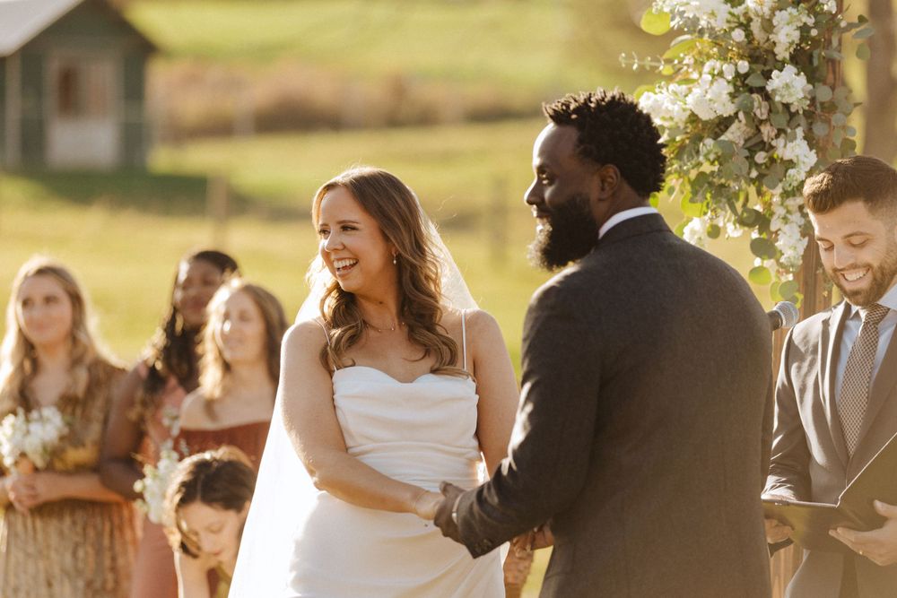 A happy couple shares a joyful moment during their outdoor wedding ceremony under blooming flowers at sunset near vernon nj.