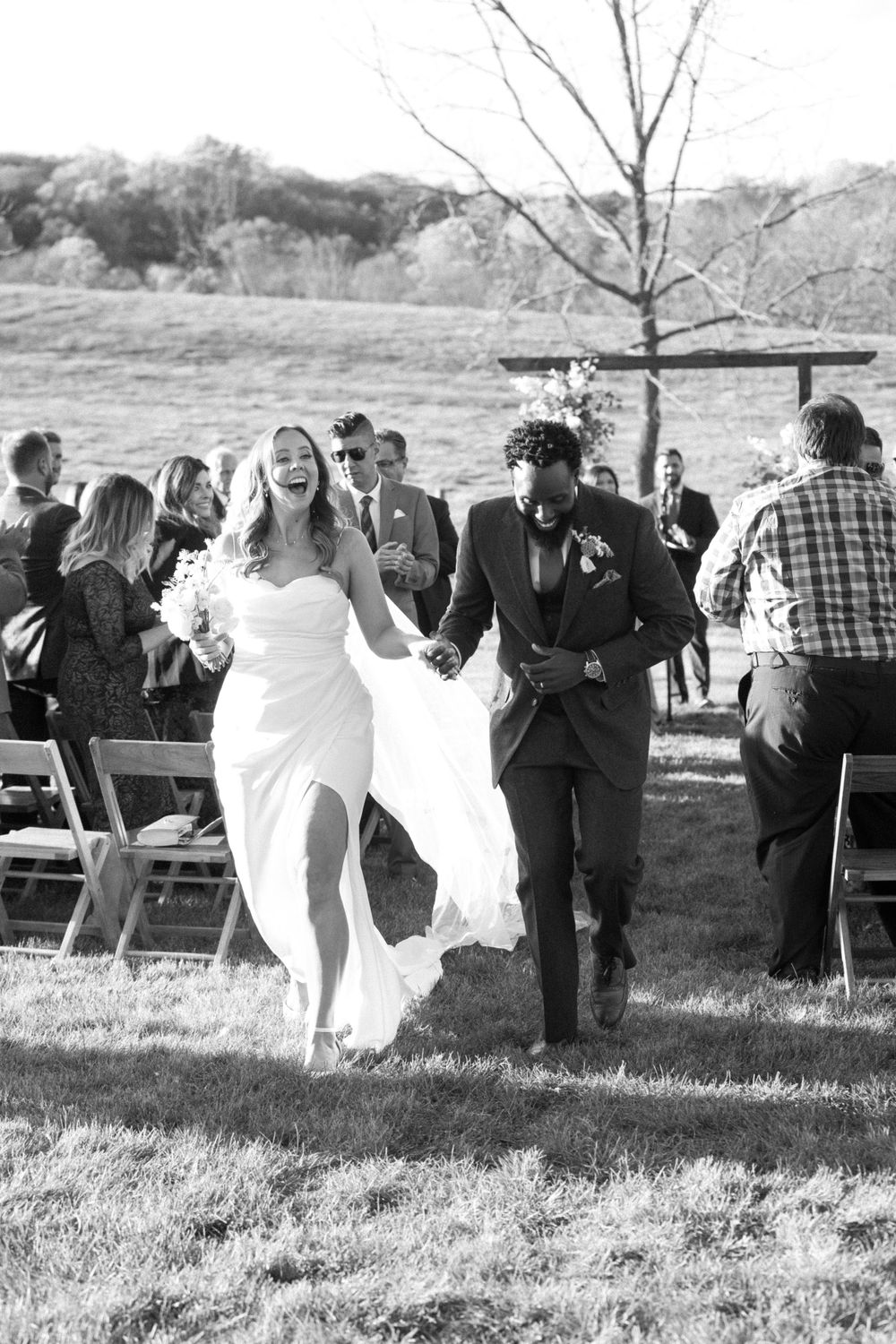 A joyful couple walking down the aisle at an outdoor wedding ceremony as guests look on in black and white photography near vernon nj.