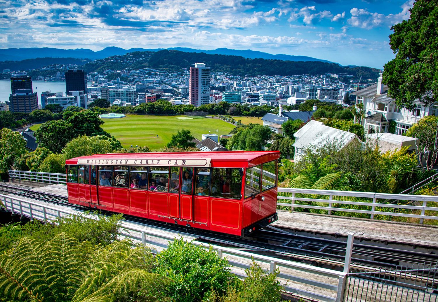 Modern city skyline with mountains and green hills under vibrant blue sky.