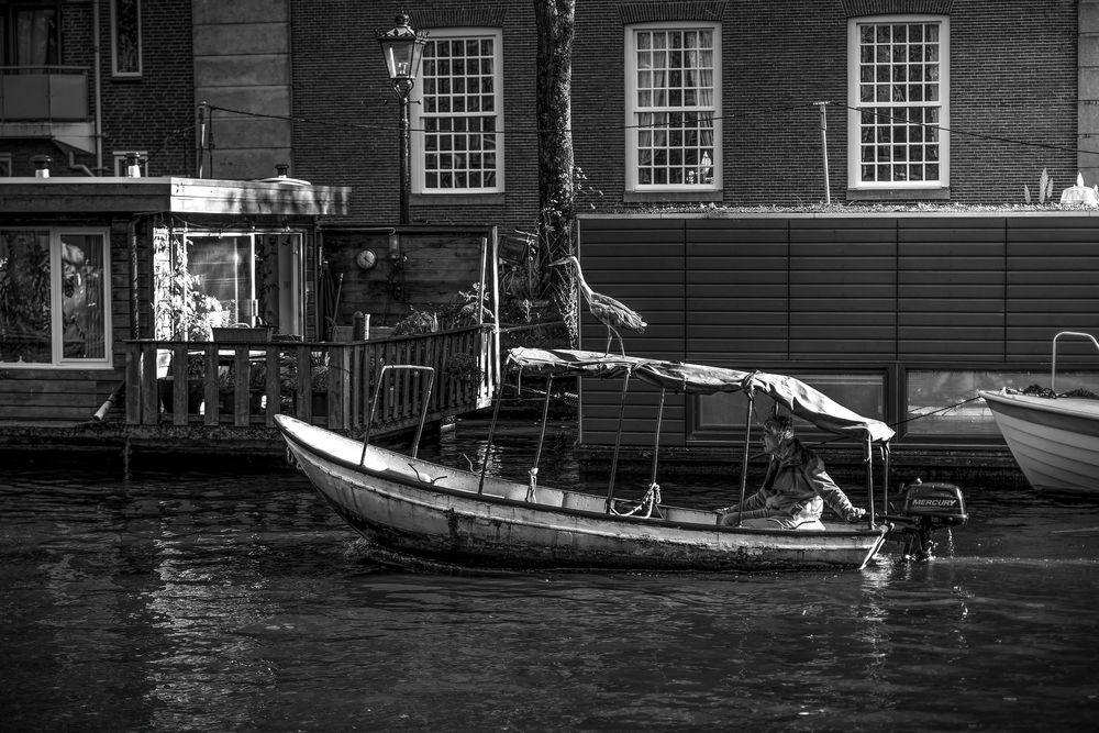 Black and white photo of a wooden sailboat moored at a dock beside a brick building on calm water.