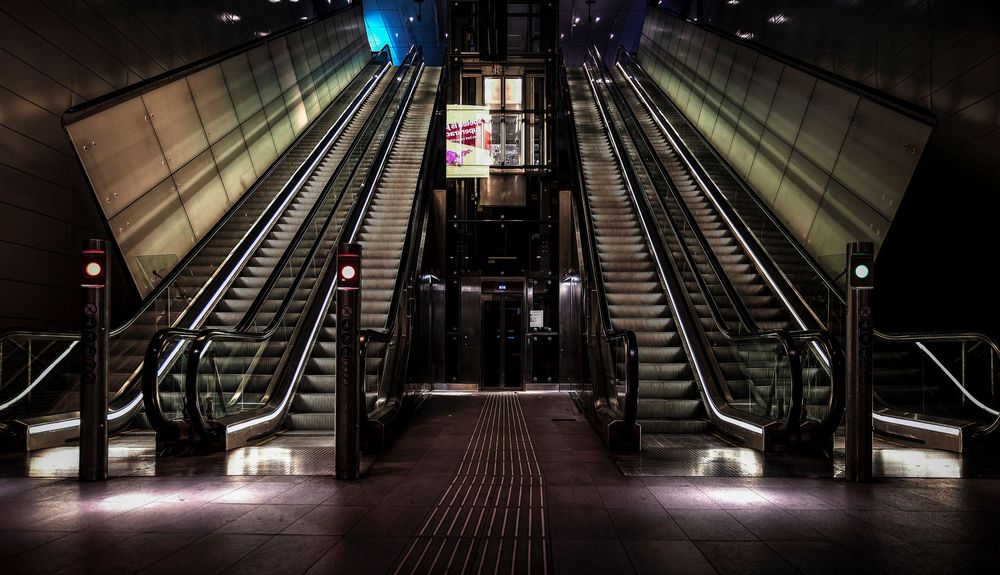 Empty subway station escalators illuminated at night with sleek modern architecture and dramatic lighting.