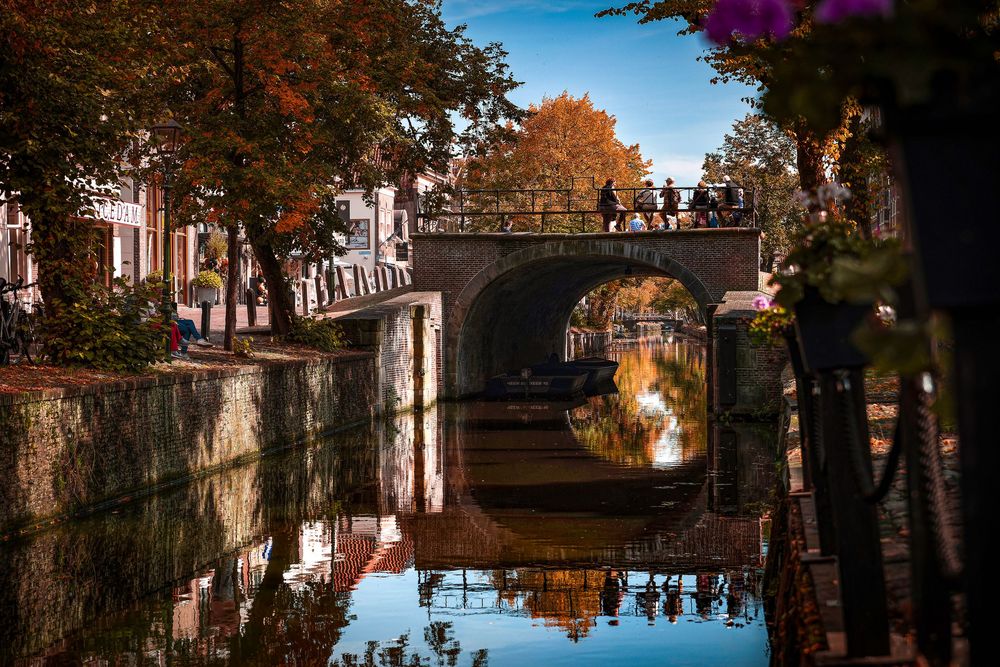 Autumn canal scene with stone bridge reflection in still water, colorful fall foliage lining the banks.