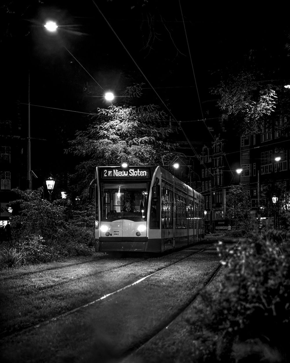 Black and white night photo of tram number 2 to Nieuw Sloten on illuminated city street.