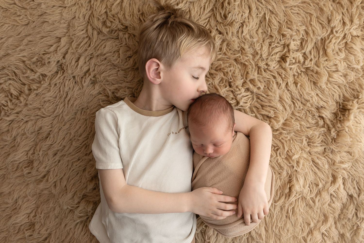 Peaceful portrait of two siblings cuddling on soft beige rug during intimate photoshoot.