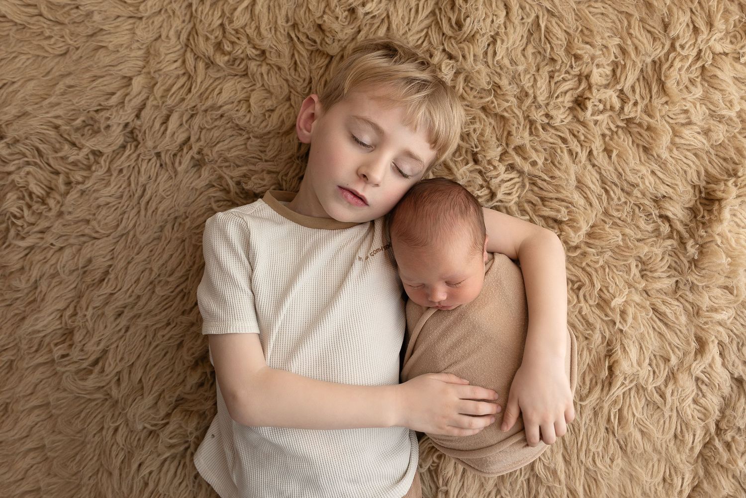 Two children lying together on a soft beige carpet in tender embrace.