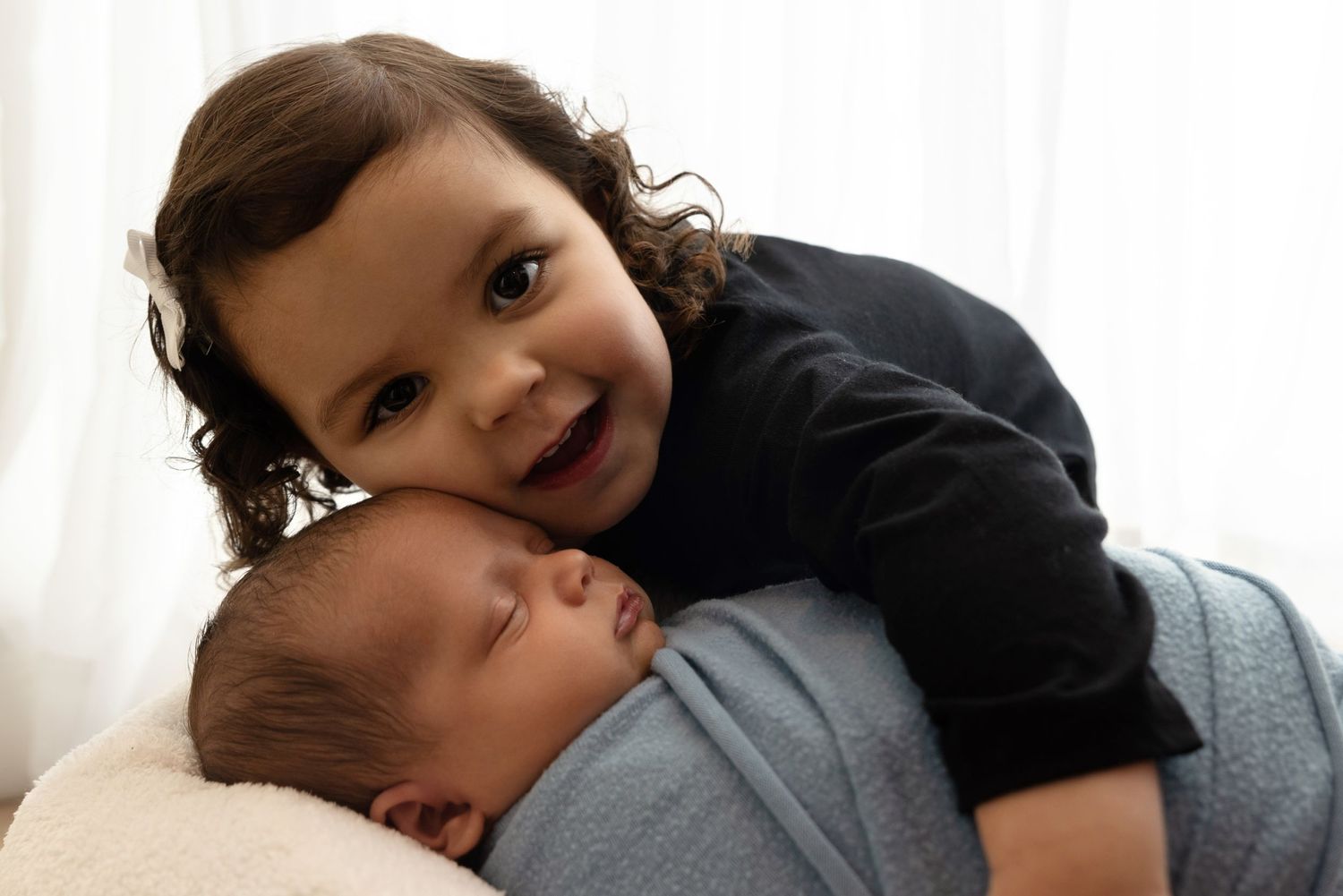 Two young children share a sweet moment together while resting on white bedding.