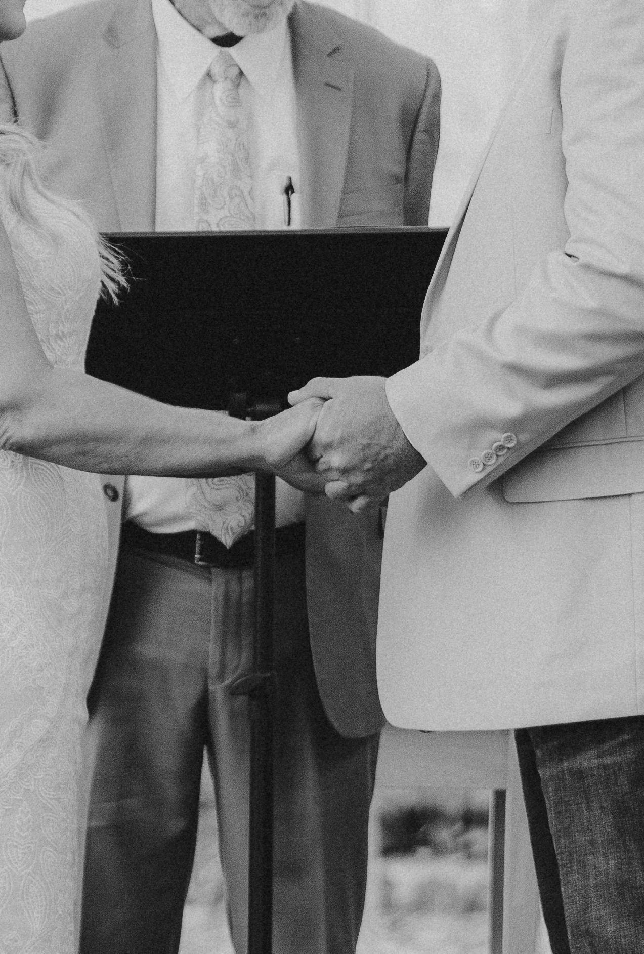 Black and white photo showing hands holding a binder during a wedding ceremony.
