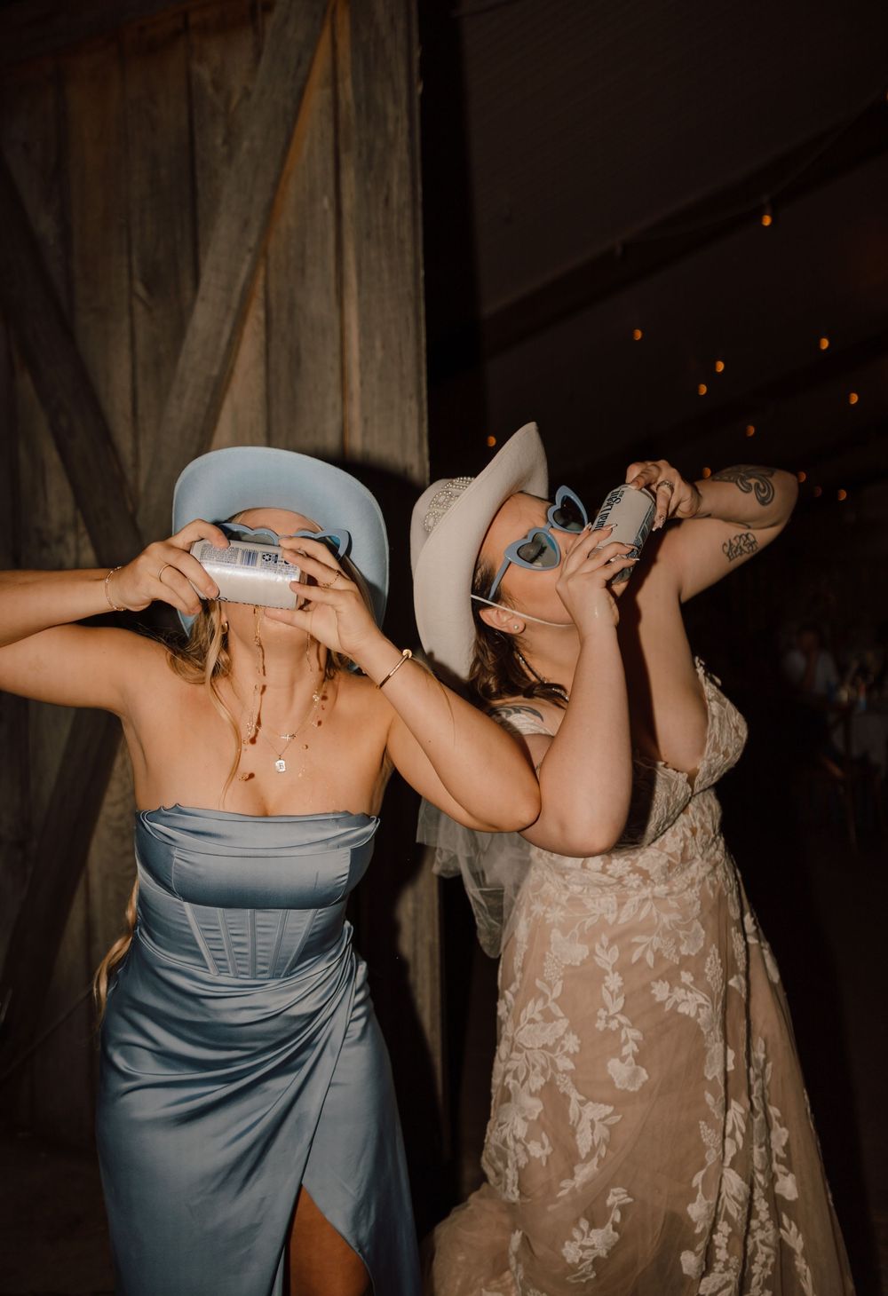 Two women in elegant dresses taking shots together at what appears to be a wedding reception or party.