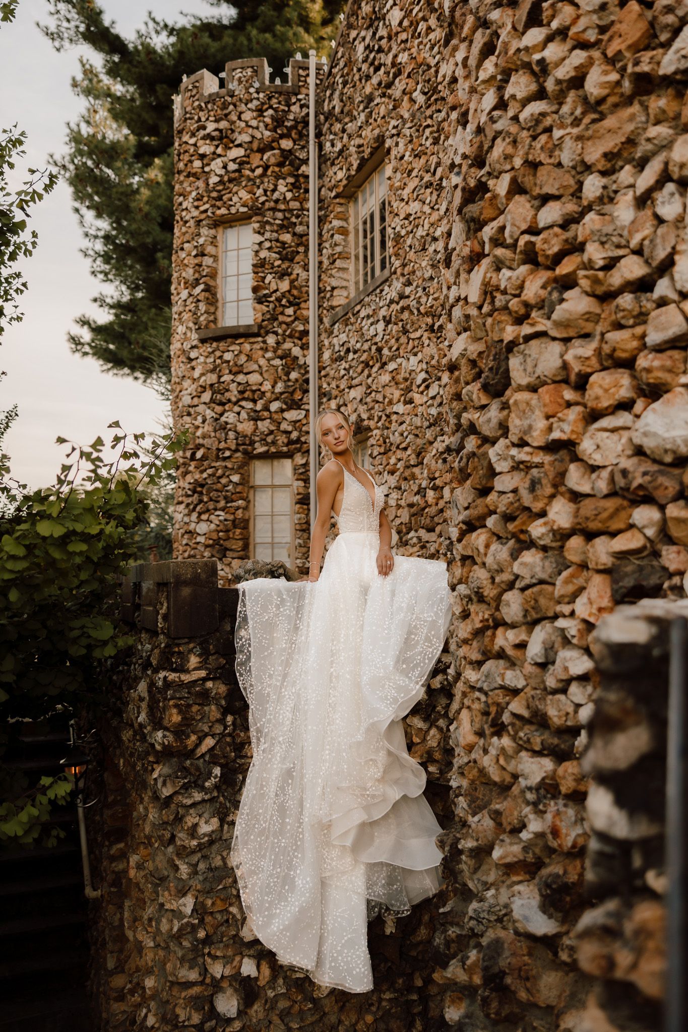 White wedding dress displayed against rustic stone wall in natural outdoor setting for bridal detail photography.