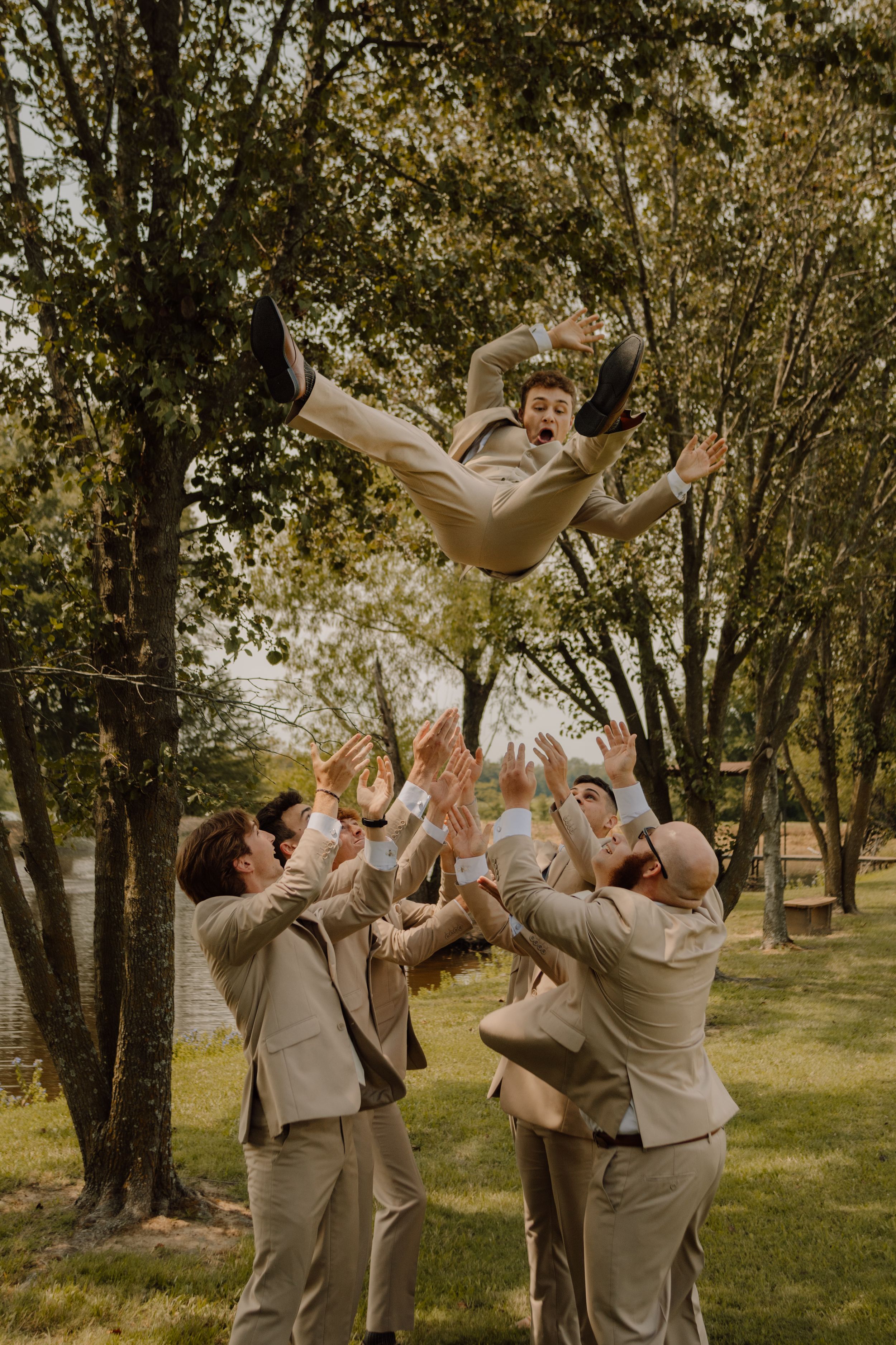 Groomsmen toss someone in the air during outdoor wedding festivities.