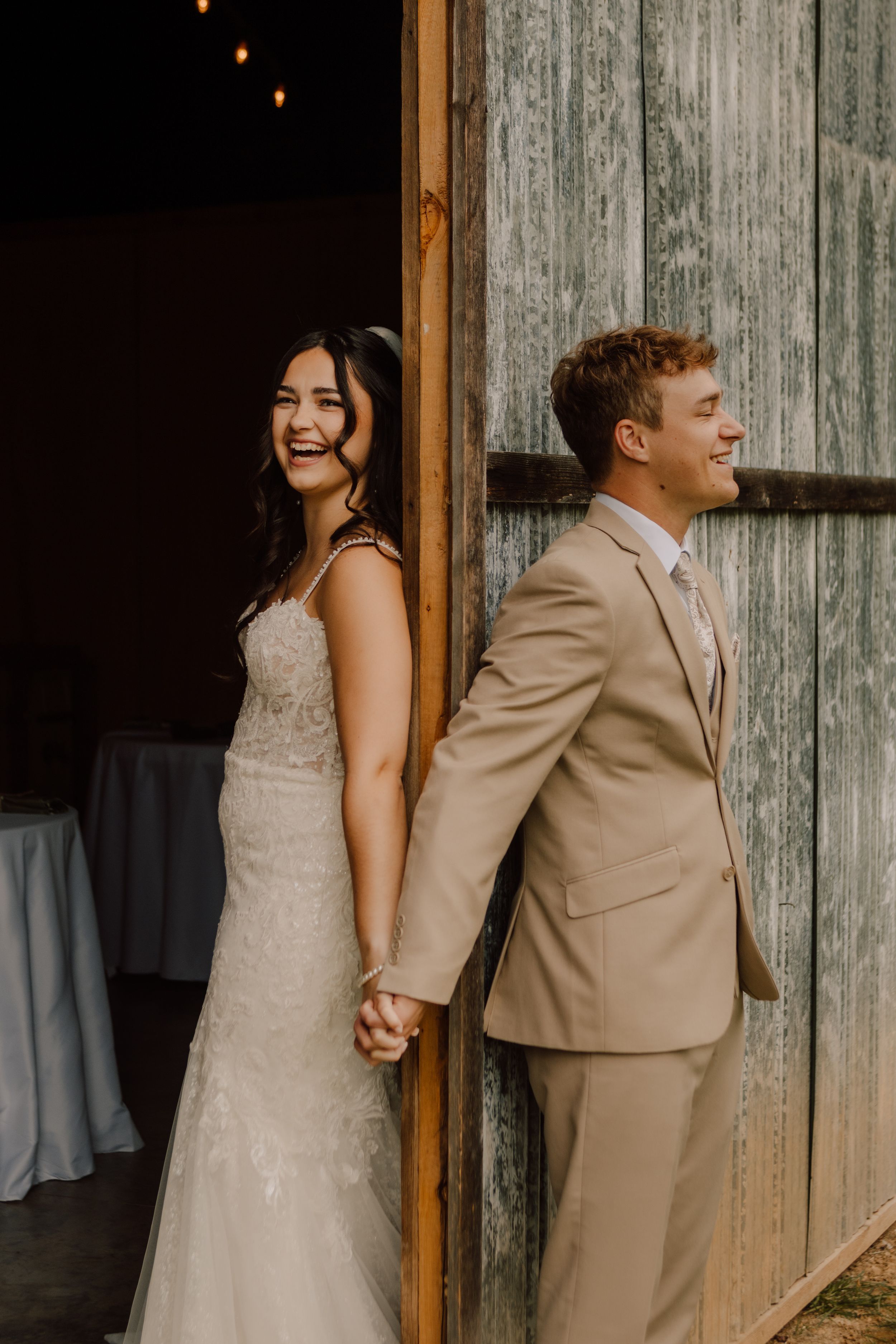 A couple shares a first look moment while holding hands against a rustic barn door.