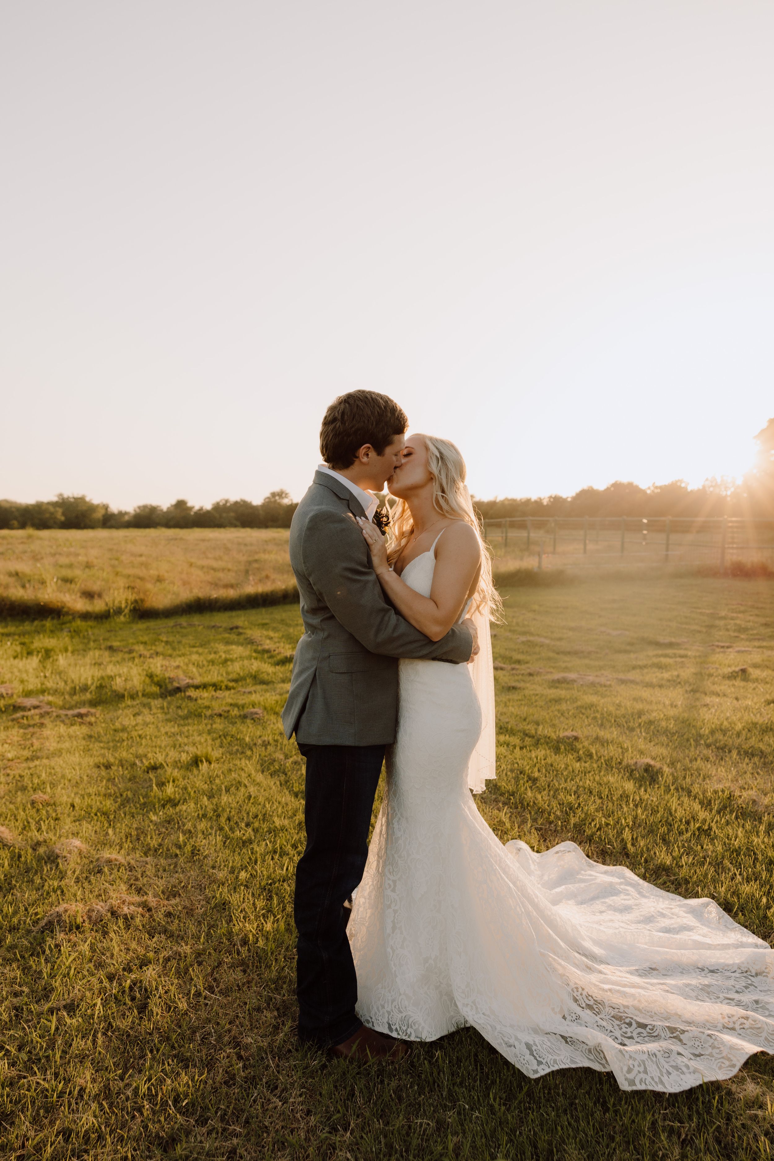 Bride and groom embrace in a sun-drenched meadow during their wedding photoshoot at sunset.