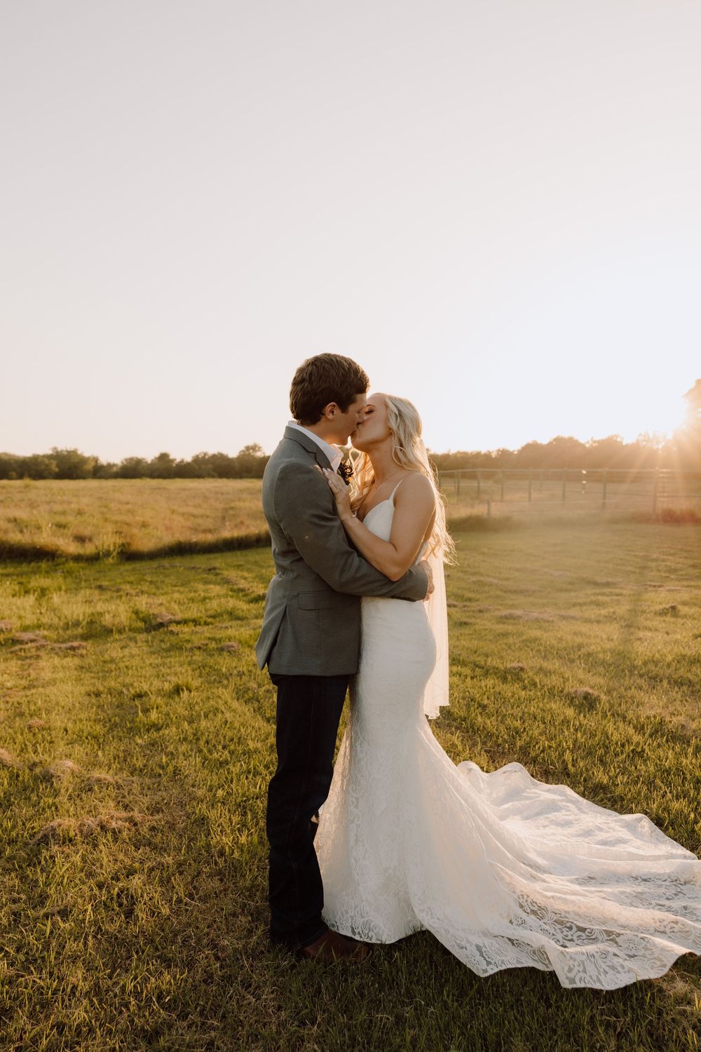 Bride and groom embrace in a sun-drenched meadow during their wedding photoshoot at sunset.