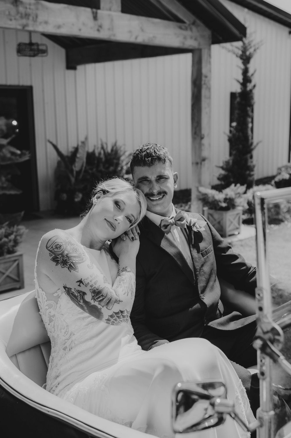 A couple shares a candid romantic moment together outdoors while relaxing on patio furniture in black and white.