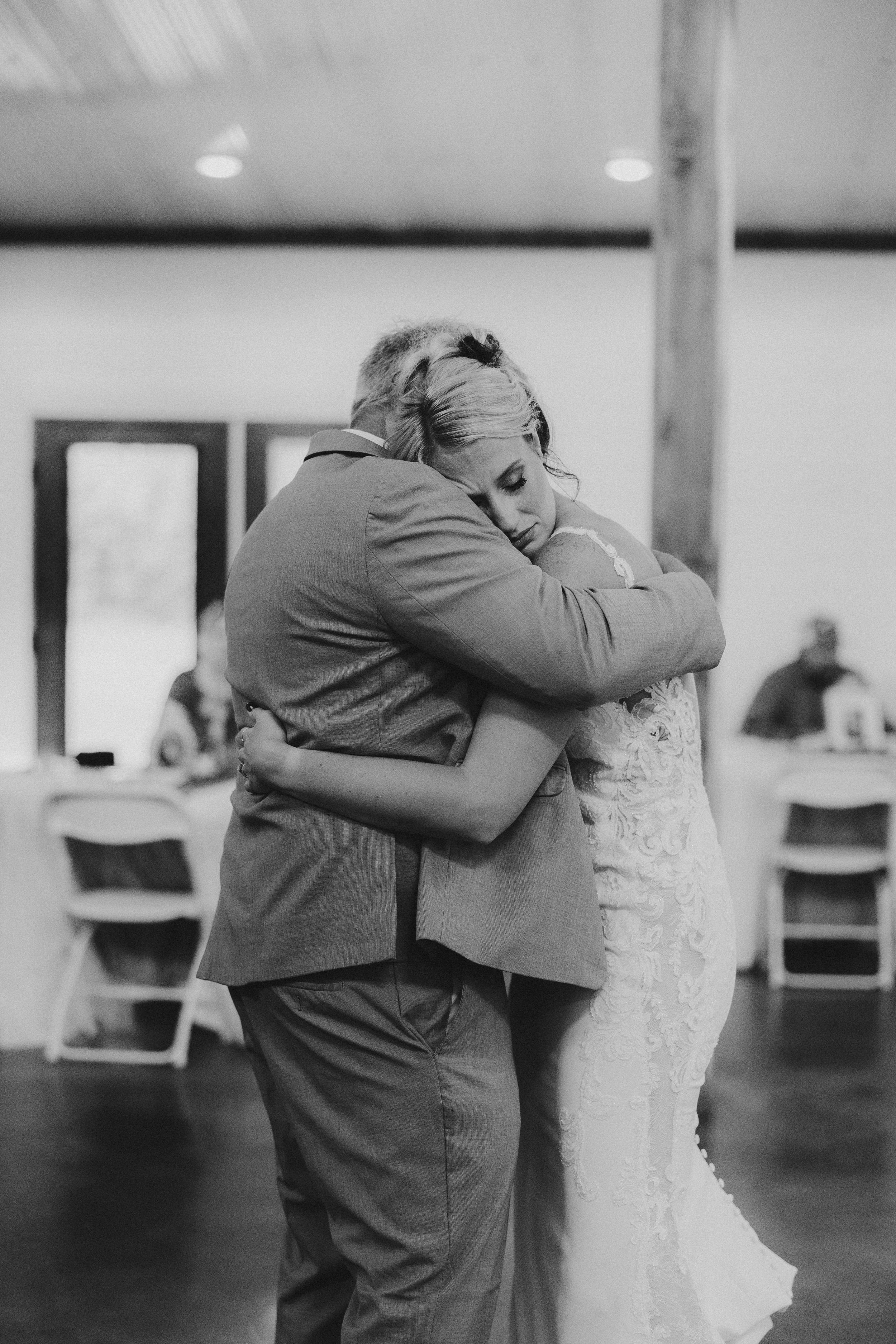 A tender embrace on the dance floor at a wedding reception, with guests visible in the background.