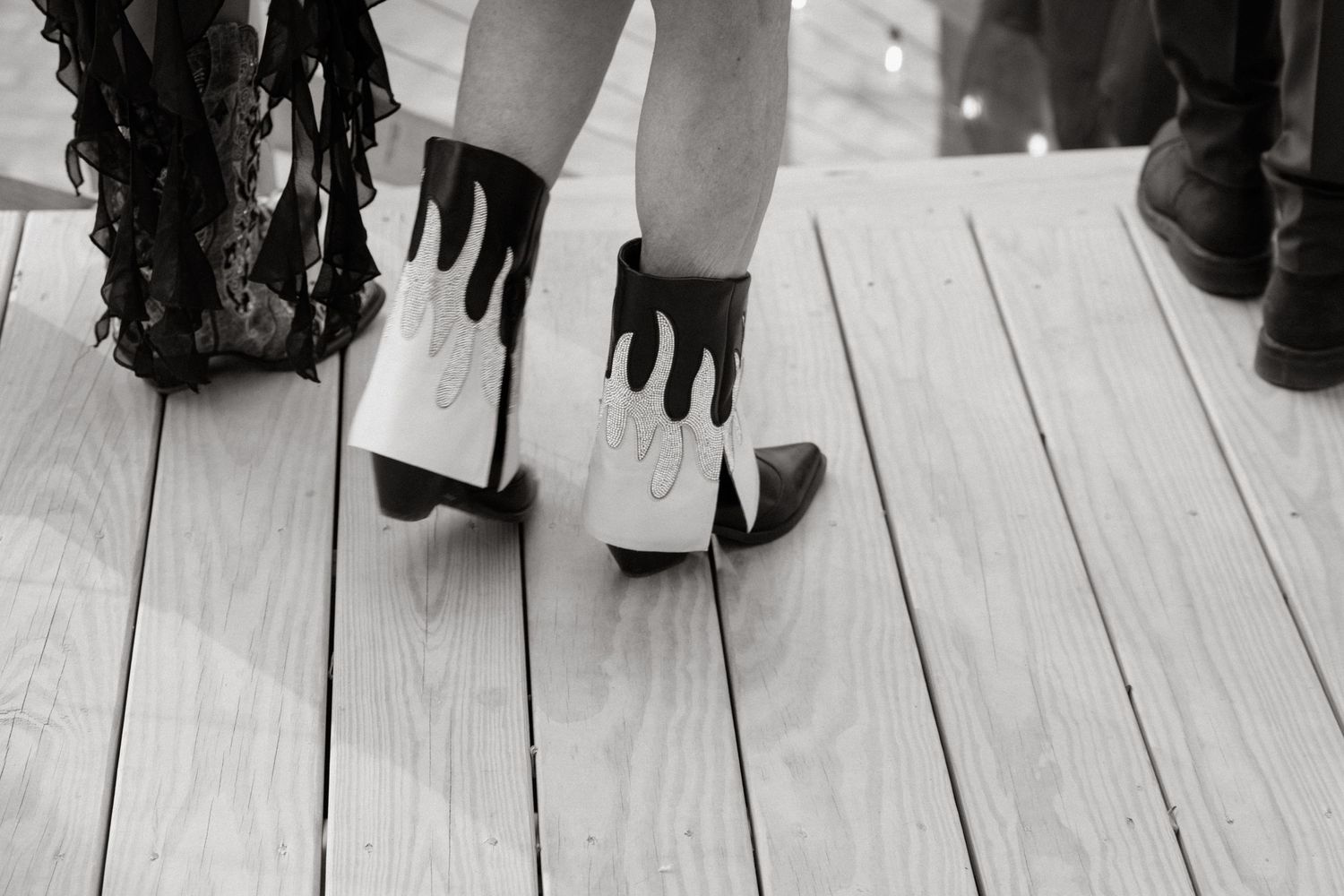 Black and white image of feet in gloves walking on wooden deck planks.
