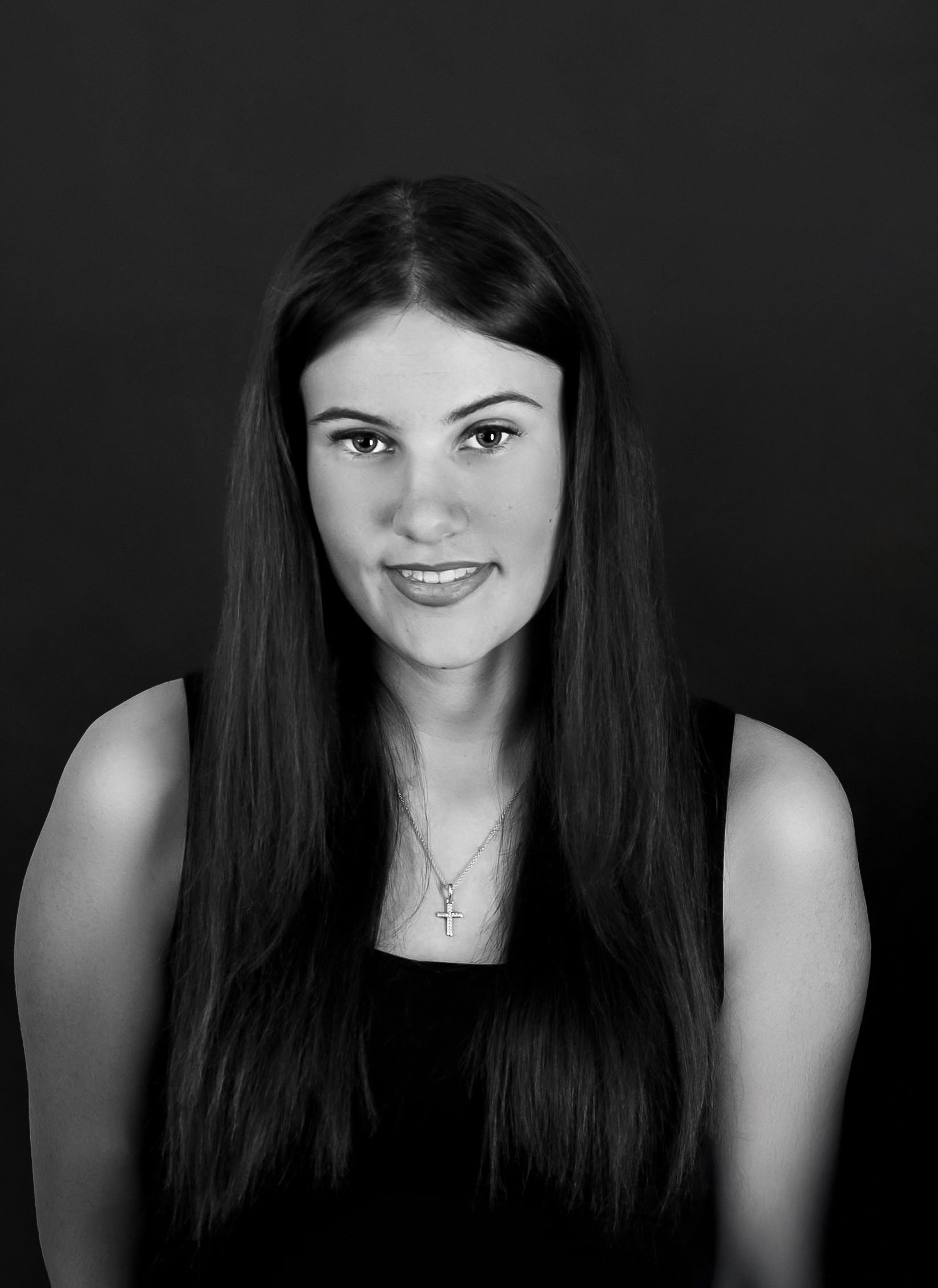 A black and white portrait photo shows a smiling woman with long dark hair wearing a dark sleeveless top and small necklace.