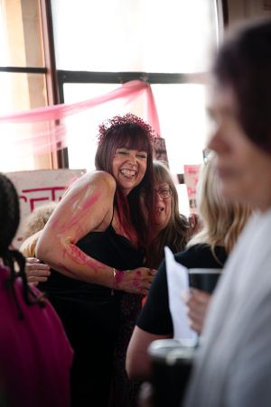 People laughing and celebrating at a social gathering with pink lighting and a warm indoor atmosphere for Kat Shaw's Art Exhibition.