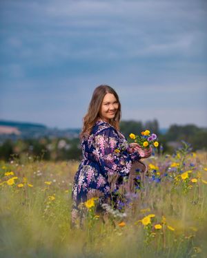 A person in a floral dress stands in a wildflower meadow with yellow blooms against a blue sky on a sunny day.