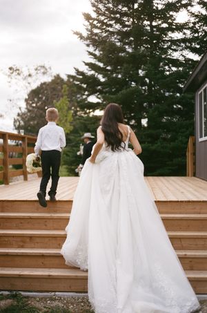 Wedding couple ascending wooden deck stairs outdoors with pine trees in the background.