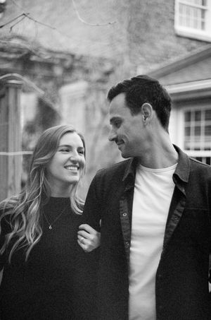 A couple sharing a joyful moment together outdoors in black and white, both wearing dark sweaters.