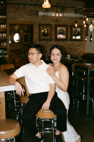 A stylish couple sits together at a vintage bar with exposed brick walls and hanging pendant lights creating a warm ambiance.
