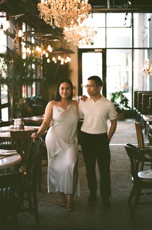 A couple poses together in an elegant restaurant interior with crystal chandeliers and ambient lighting.
