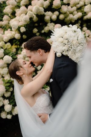 Romantic wedding couple shares tender moments against backdrop of white hydrangea flowers in garden setting.