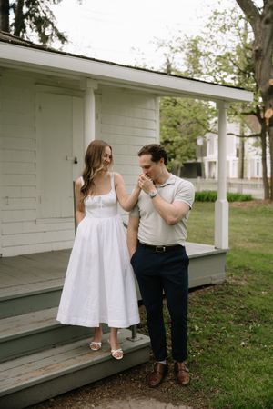 Two people share a tender moment on the steps of a white porch on a summer day.