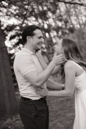 A romantic black and white photo of a couple laughing and embracing outdoors in a natural setting with bokeh background.