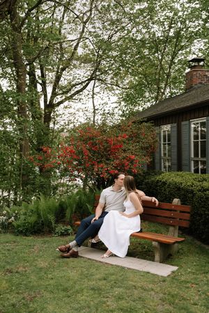 A couple shares a romantic moment on a garden bench by a cottage with blooming red azaleas and lush greenery.