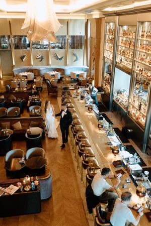 Upscale restaurant interior with long bar counter, illuminated display shelves, and modern decor featuring herringbone wood floors.