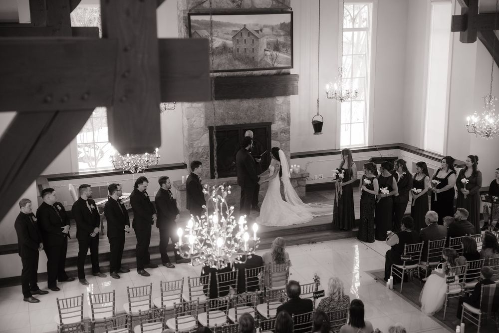 Wedding guests seated in rows of white chairs inside an elegant chapel with natural light streaming through windows.