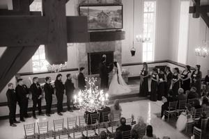 Wedding guests seated in rows of white chairs inside an elegant chapel with natural light streaming through windows.
