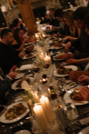 Candlelit dinner table with multiple plates of food and guests gathered around in a dimly lit restaurant setting.