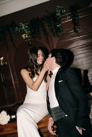 Intimate moment between couple at wedding celebration with greenery decor and wooden wall panels in background.